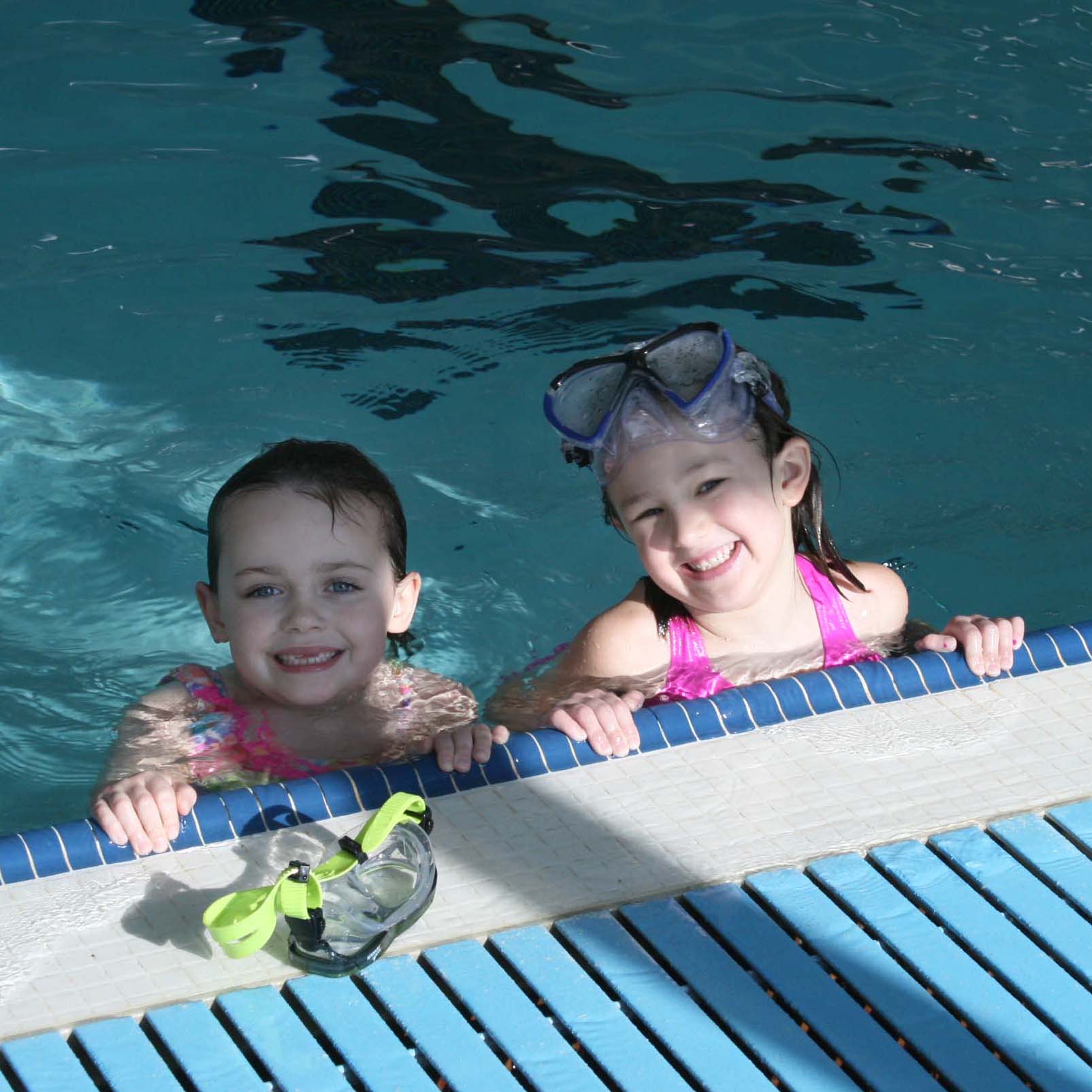 Two children in the water at the edge of the Centre pool smiling