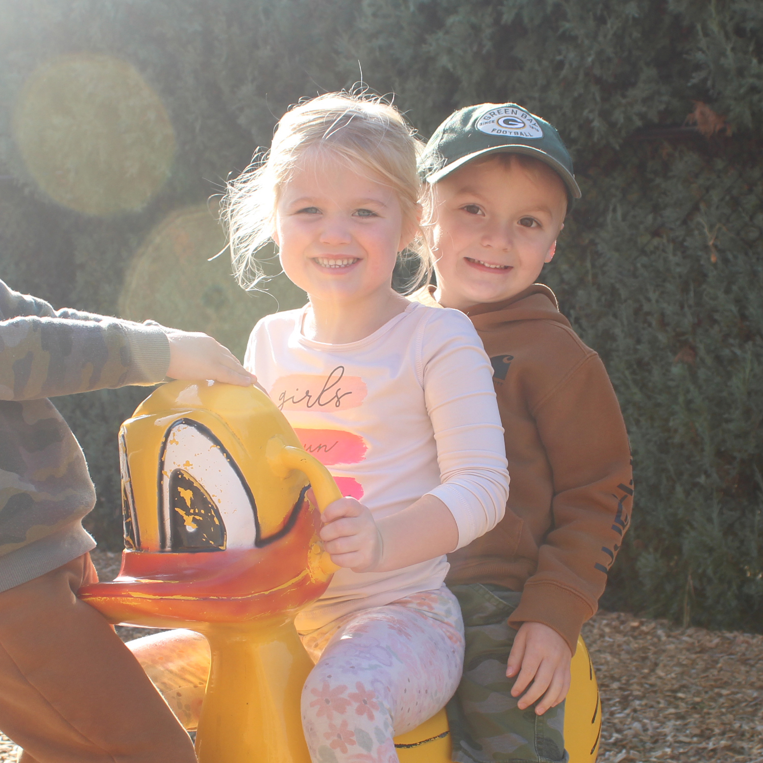 Two children smile while on a spring rider playground feature