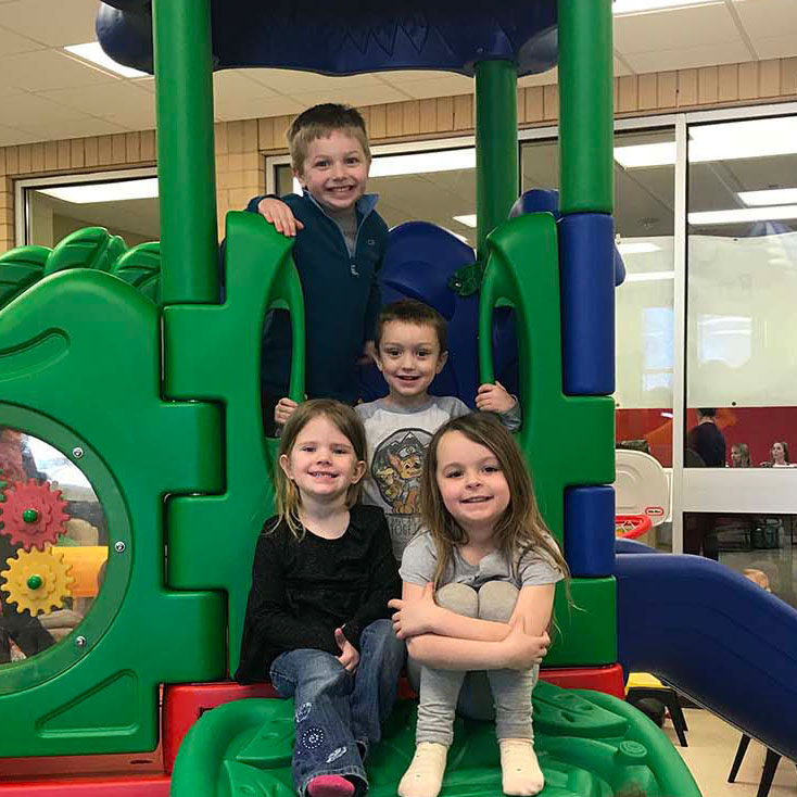 Four children on a green indoor play structure smiling