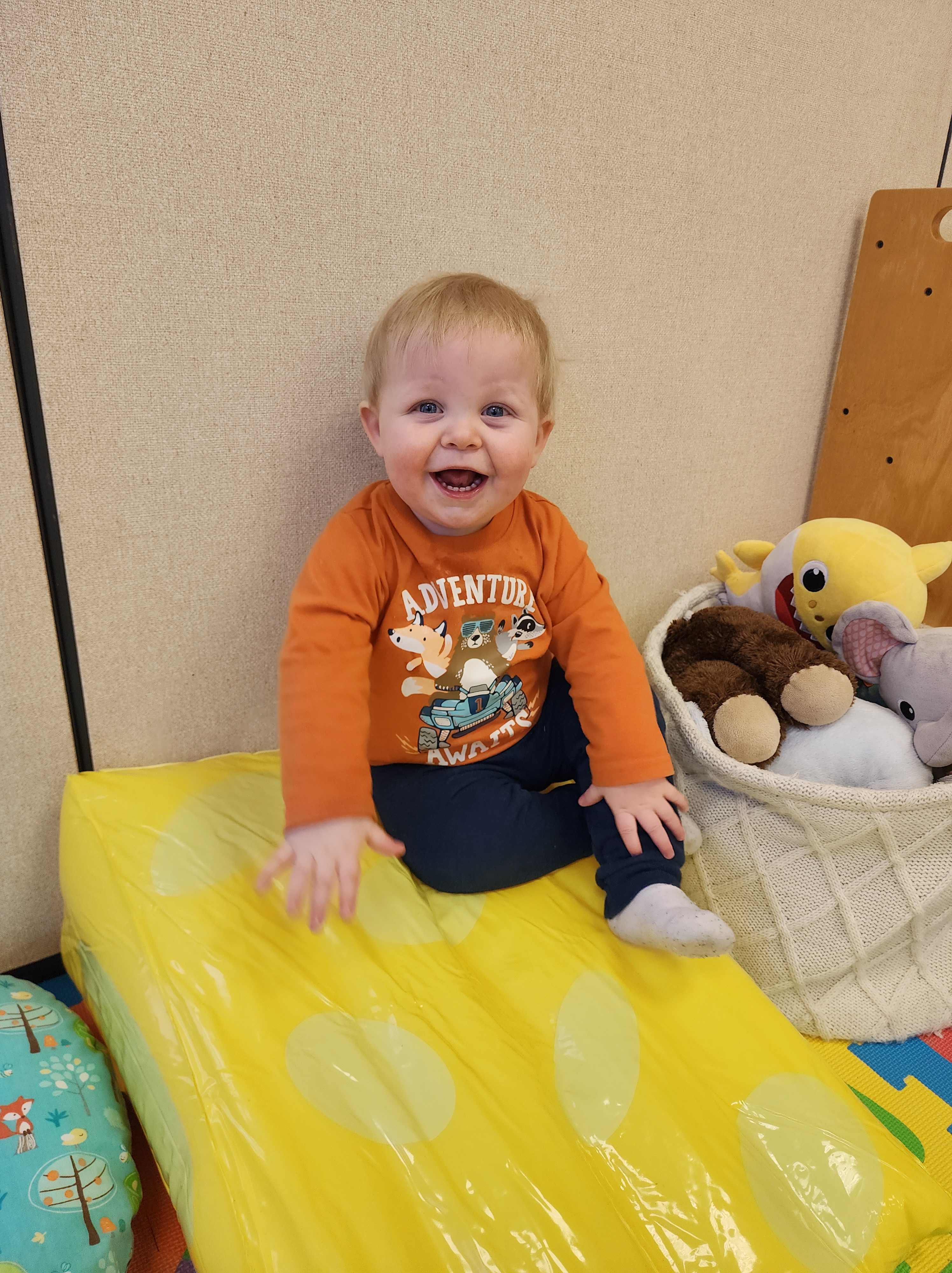 A young child sits in a playroom smiling